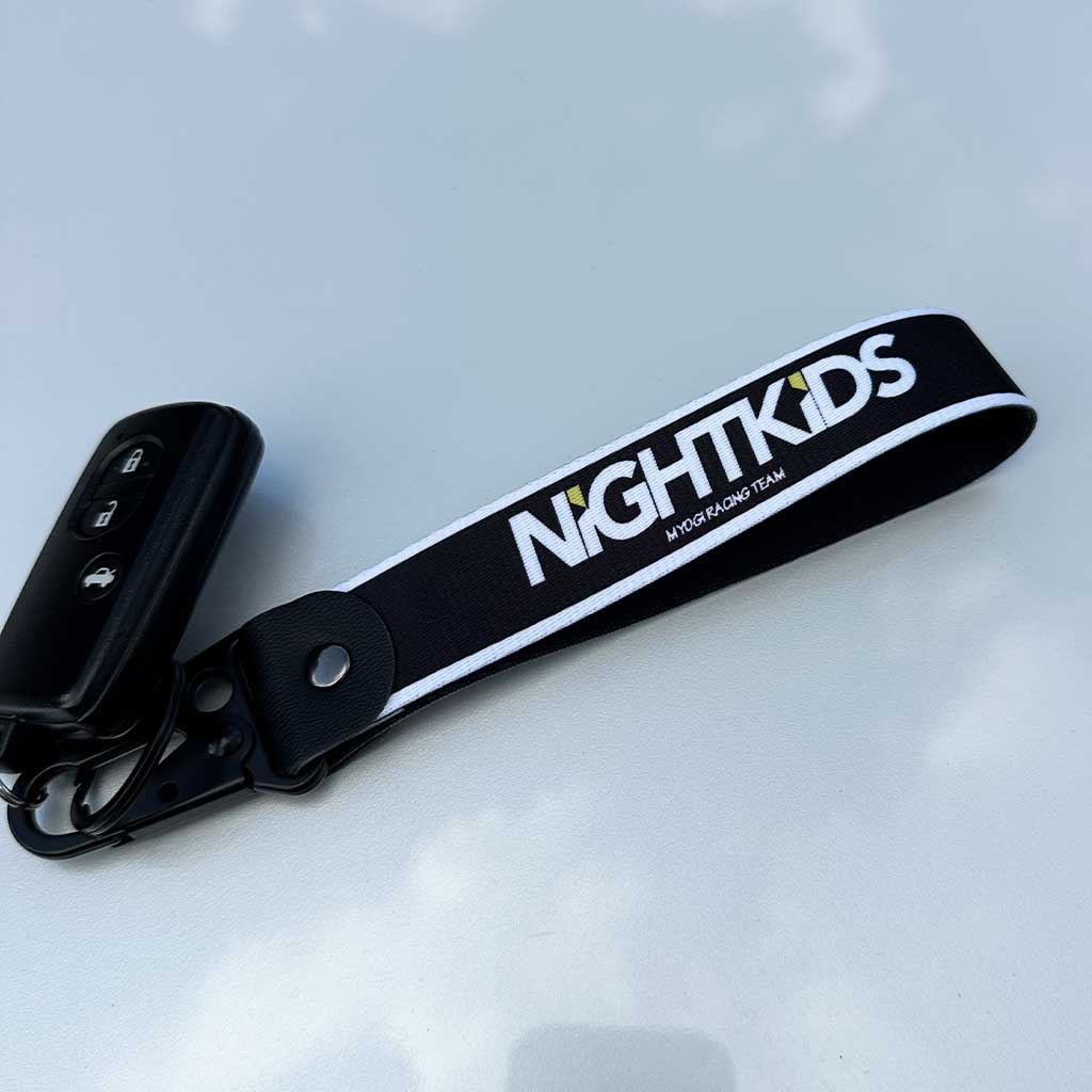 An Initial-D nightkids-themed keychain placed on a white Toyota 86's hood