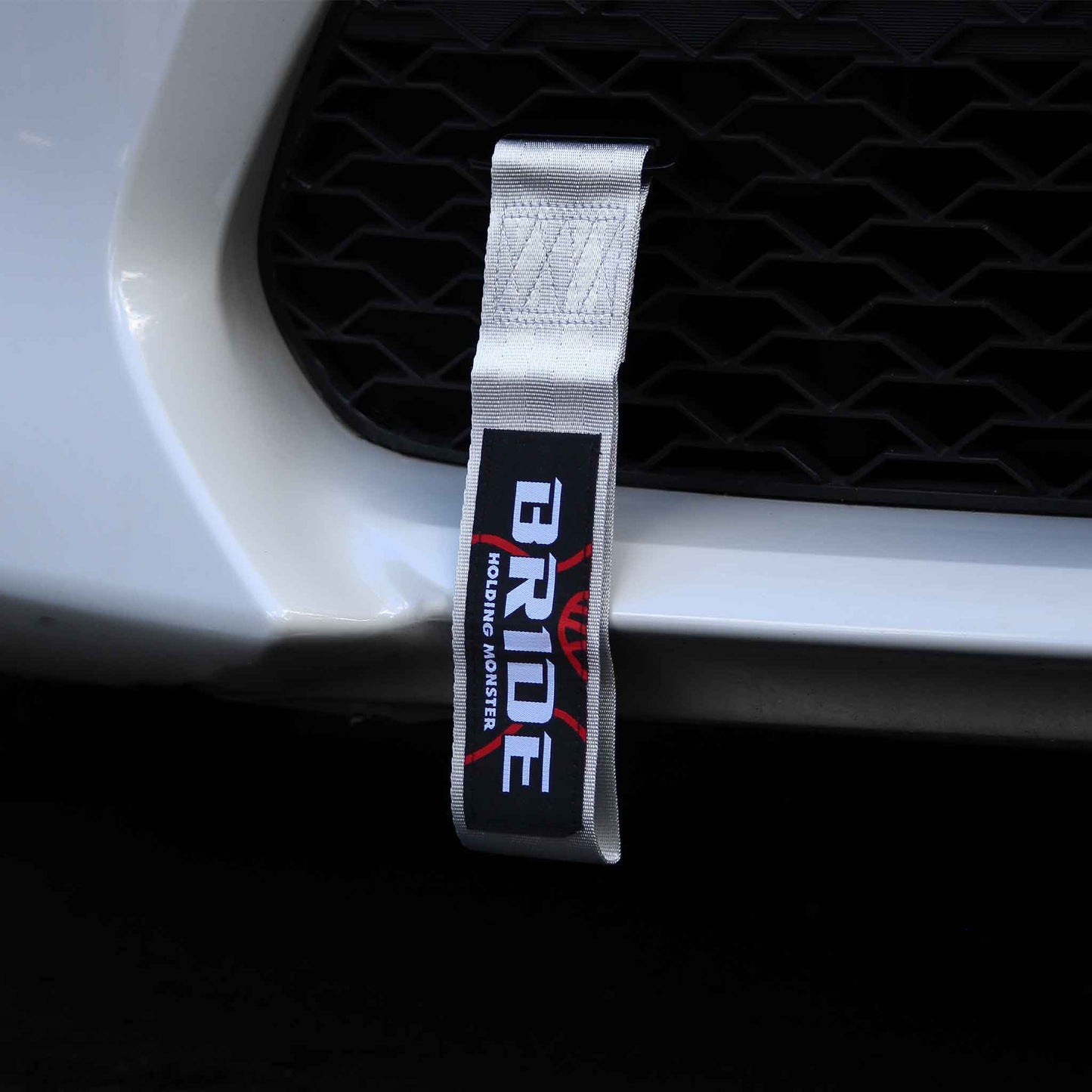 A silver BRIDE tow strap installed on a white car's front grill