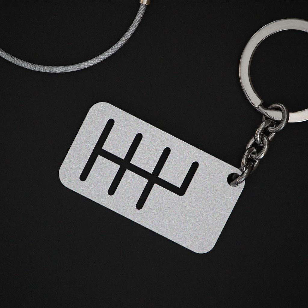 The back of a six-speed manual shift keychain with matte silver finish on a black background