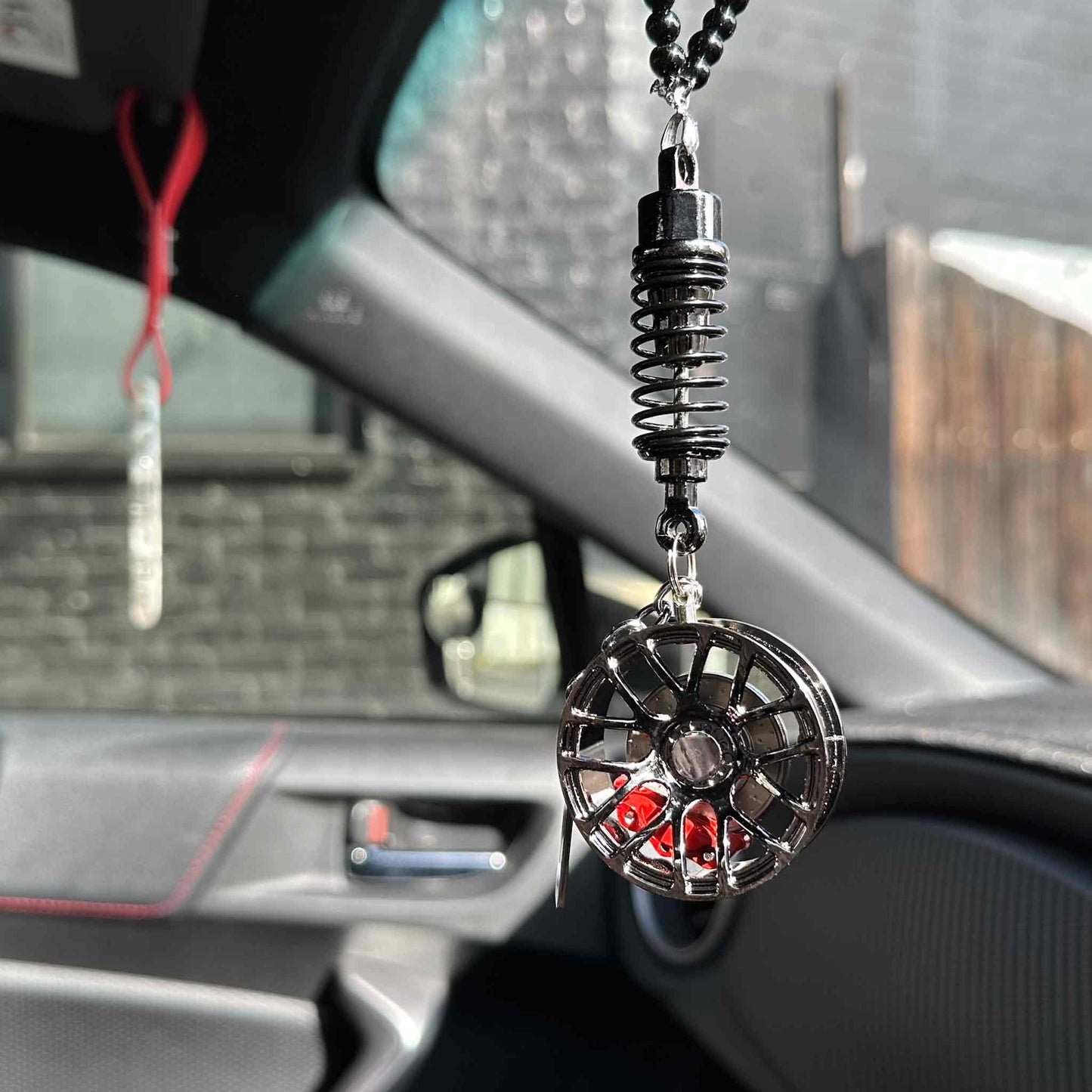 A black wheel decor hung on a car's rearview mirror in a sunny day