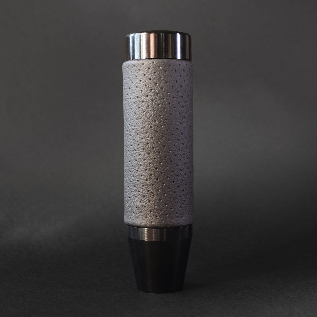 A black leather grip shift knob is standing on a dark grey floor on a dark grey background