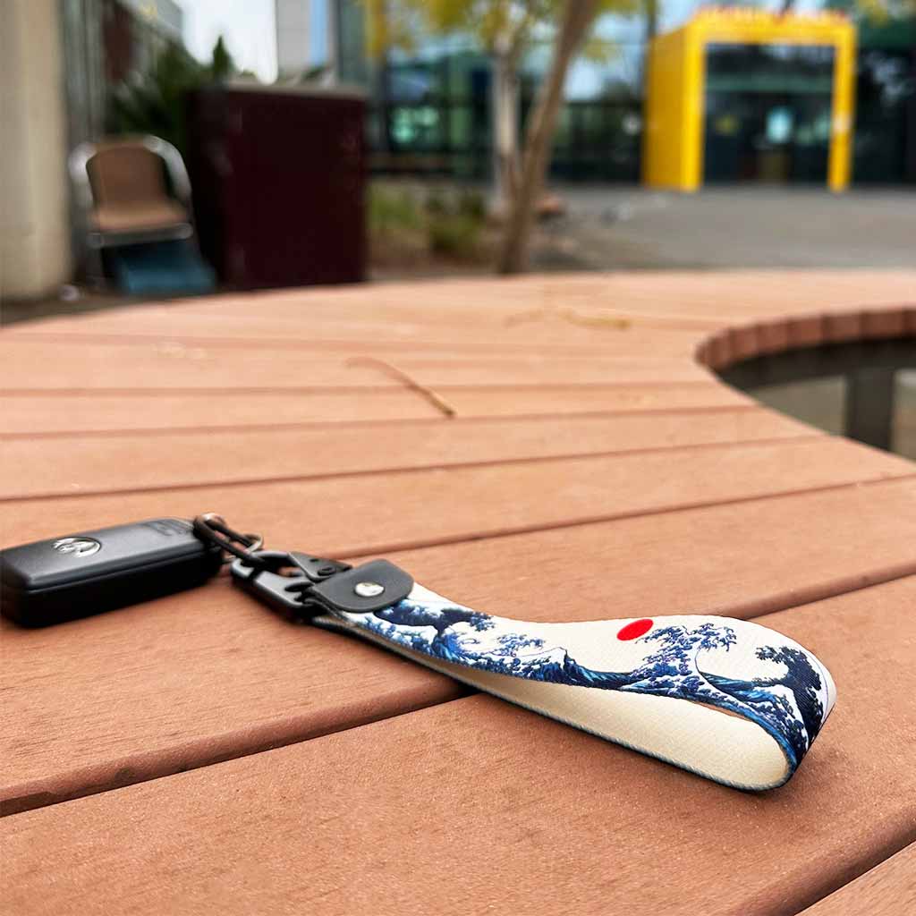 A great wave lanyard holding a Toyota car key placed on a wooden bench with treed and buildings at the back