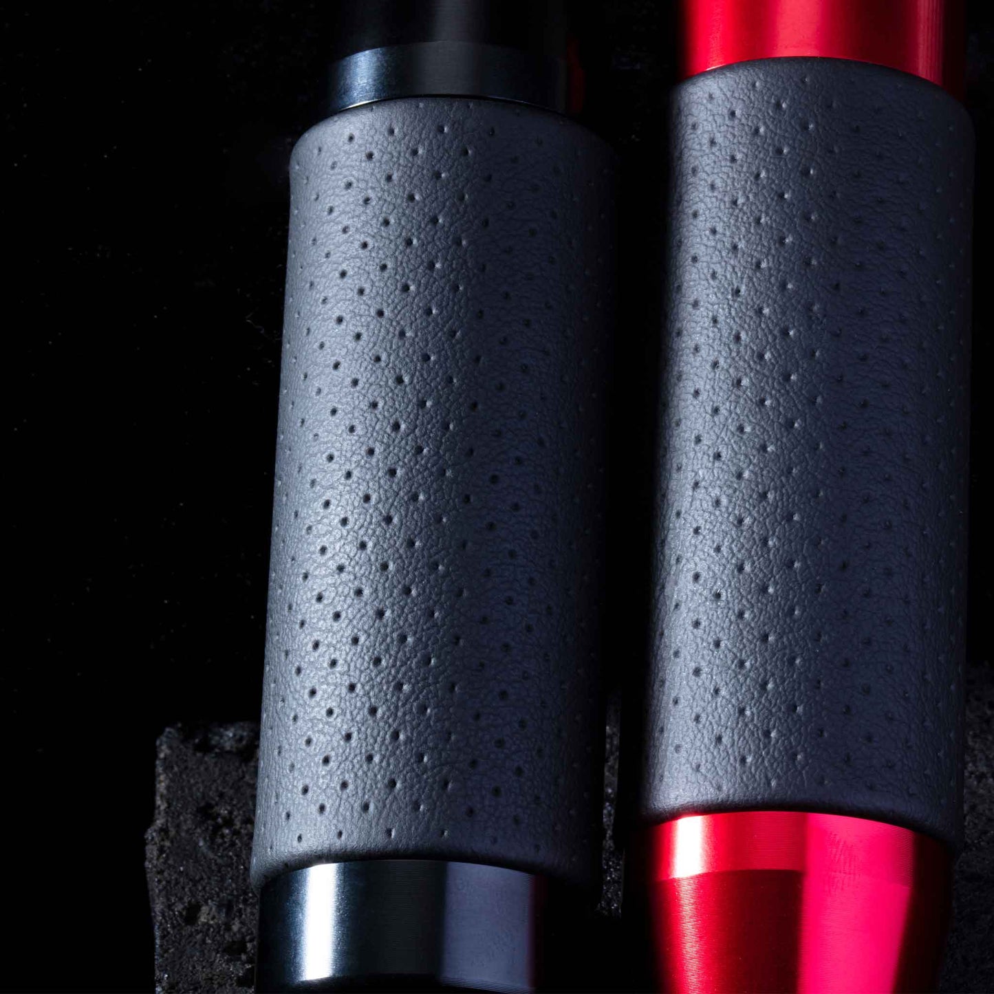 Two leather grip shift knobs are leaning closely towards a black stone on a black background, providing a closer look at the dots on the knobs