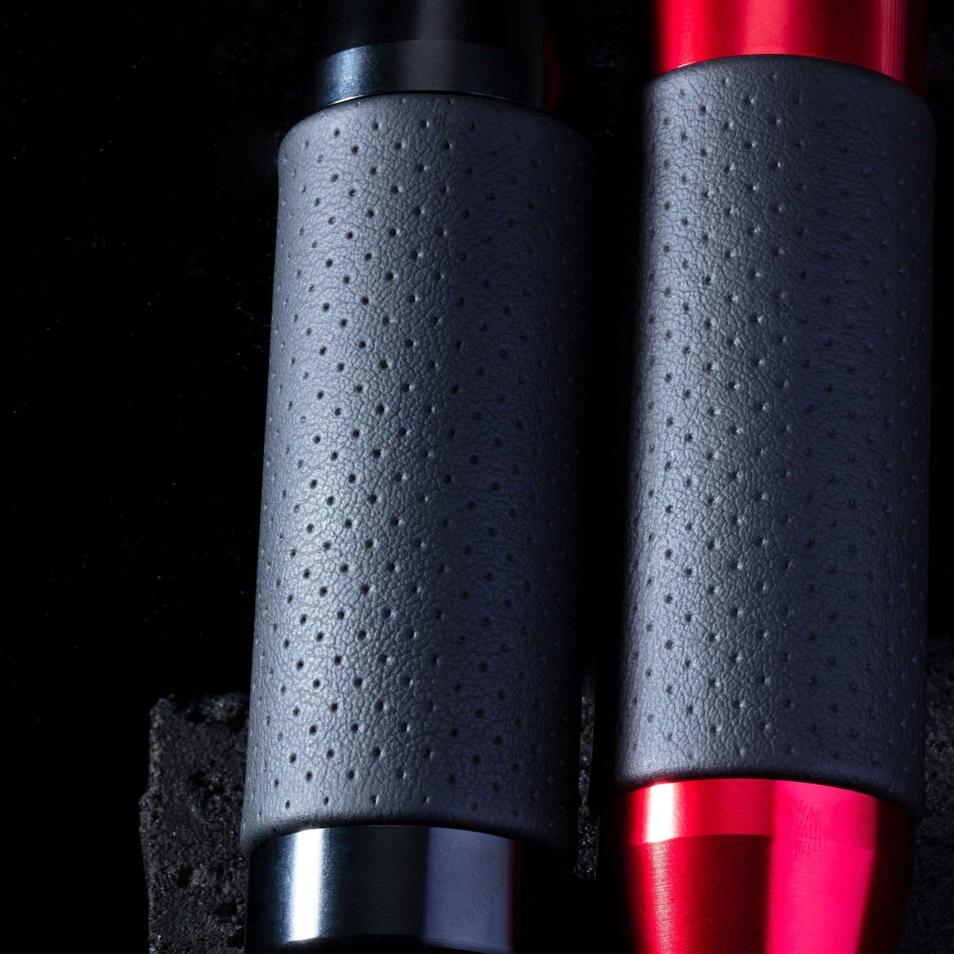 Two leather grip shift knobs are leaning closely towards a black stone on a black background, providing a closer look at the dots on the knobs