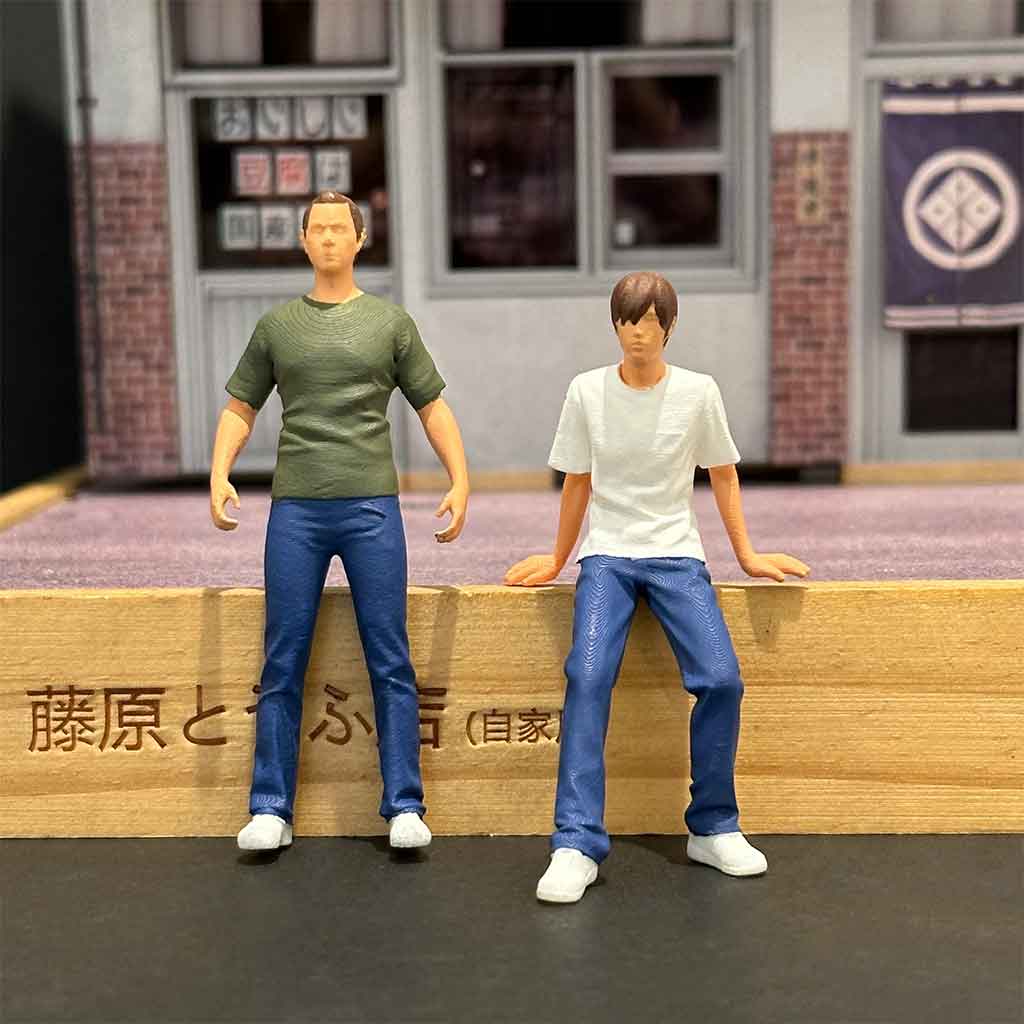 Mini figures of Fujiwara Buntai and Takumi sit on a wooden base of a Tofu Shop diorama