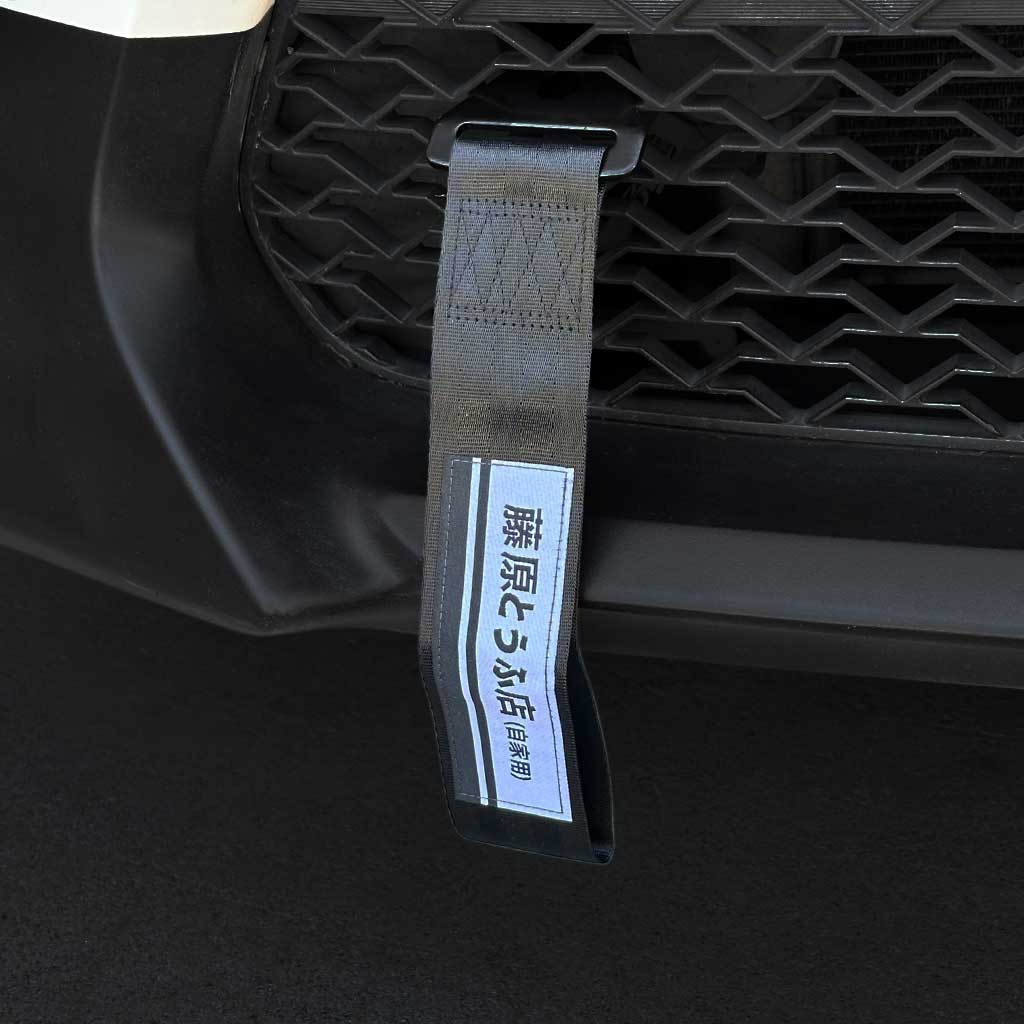A black JDM tow strap with 'Fujiwara Tofu Shop' characters installed on the front mesh of a Toyota 86
