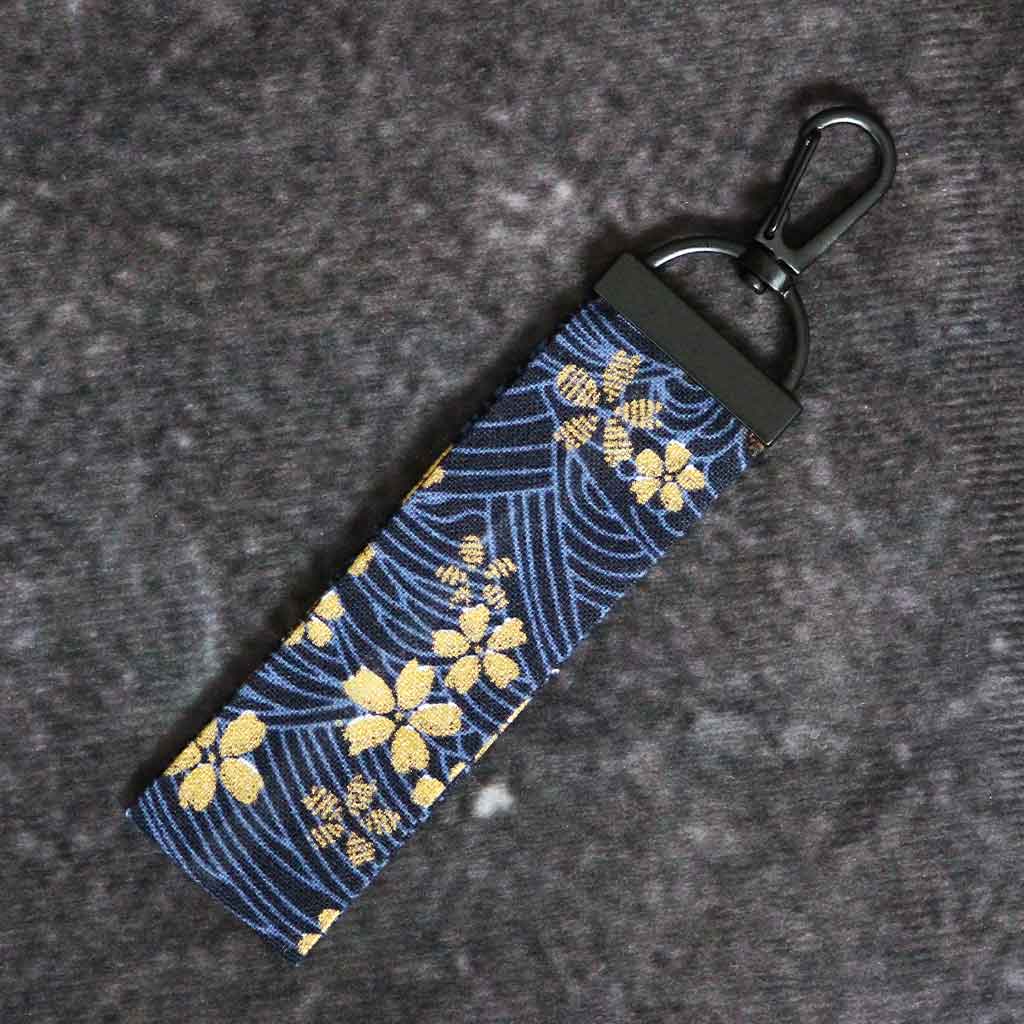 A golden cherry blossom keychain on a grey background