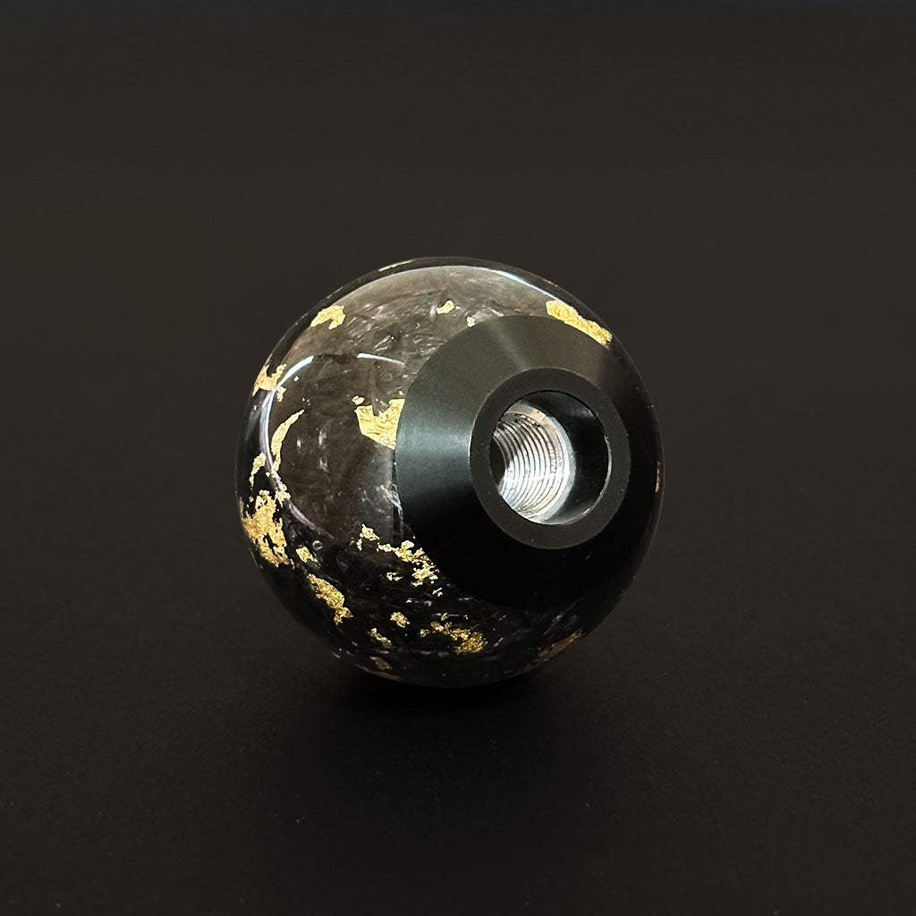 Displaying the base of a black spherical carbon fibre shift knob on a black background