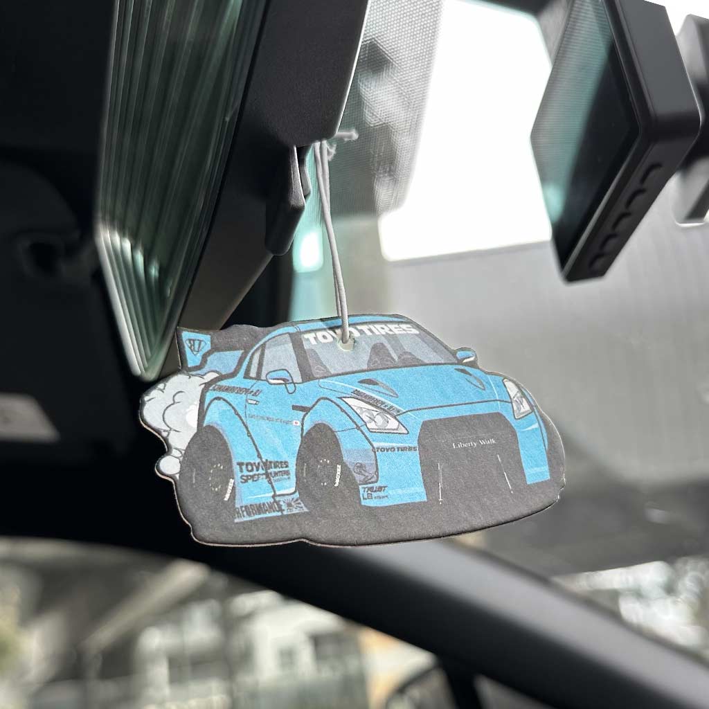 A blue GTR R35 air freshener hung on a car's rearview mirror with the rest objects blurred
