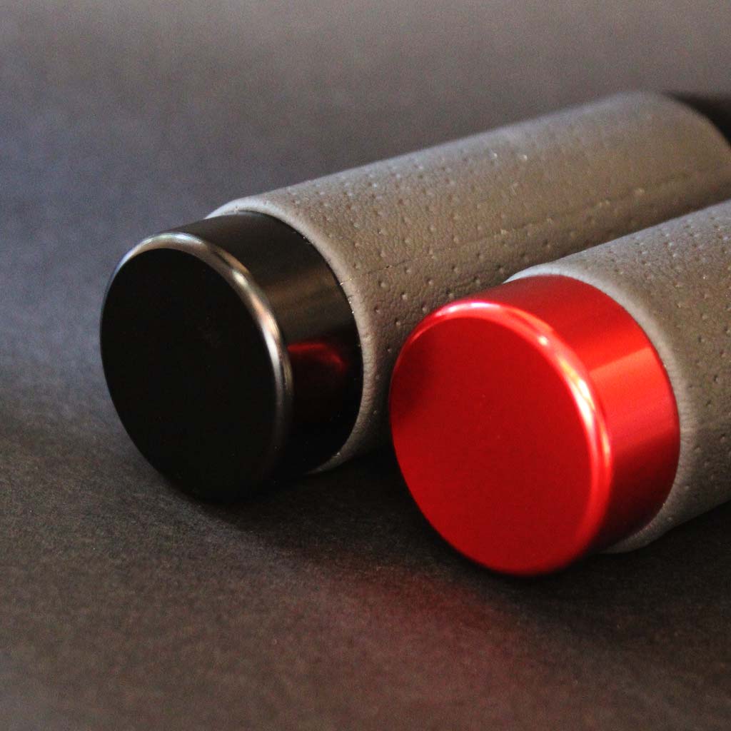 Two leather grip shift knobs are laying closely on a black floor, providing a closer look at the top section of the knobs