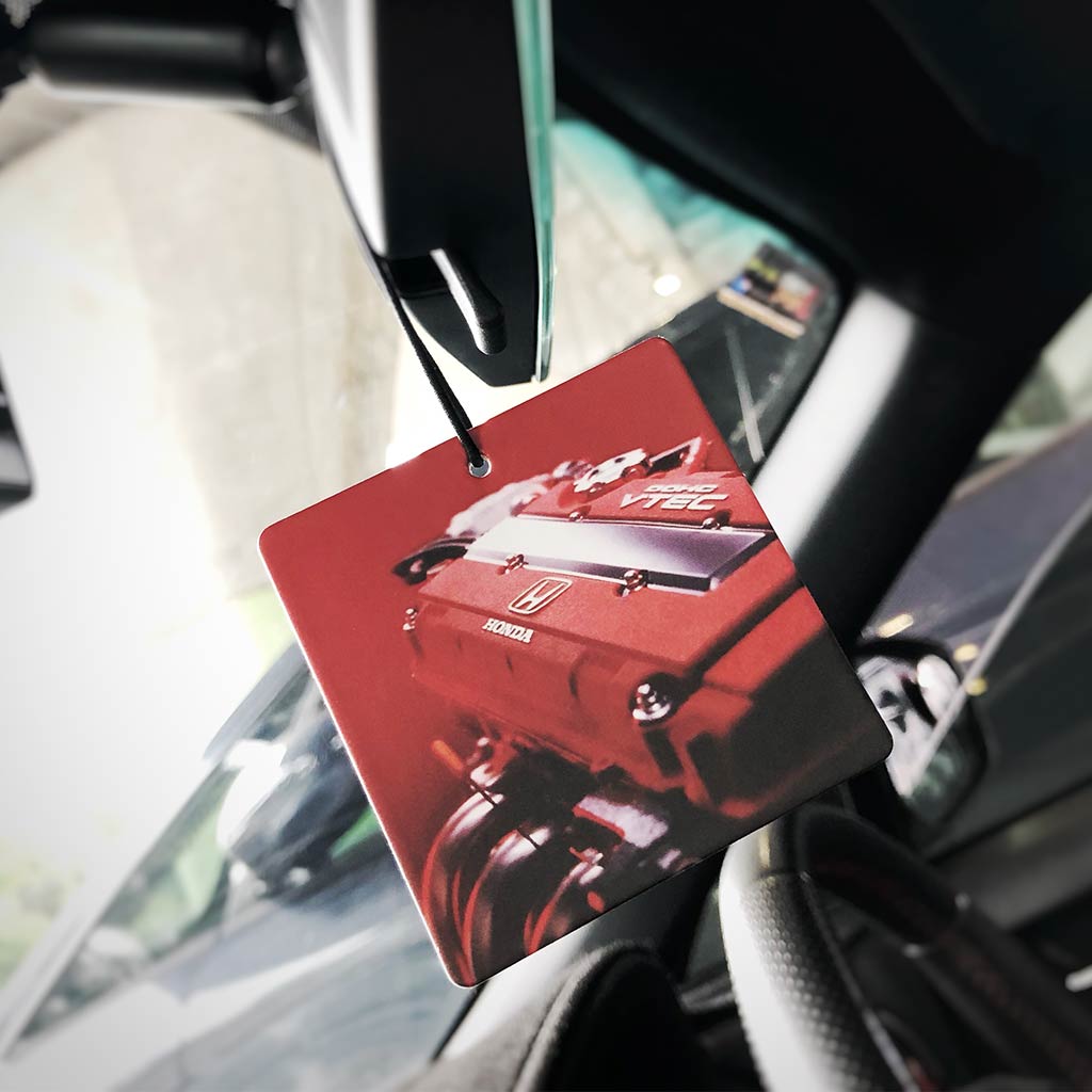 A red Honda engine air freshener hung on a car's rearview mirror
