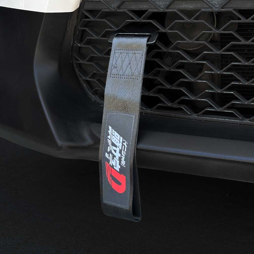 A black tow strap themed Initial-D installed on the front mesh of a Toyota 86