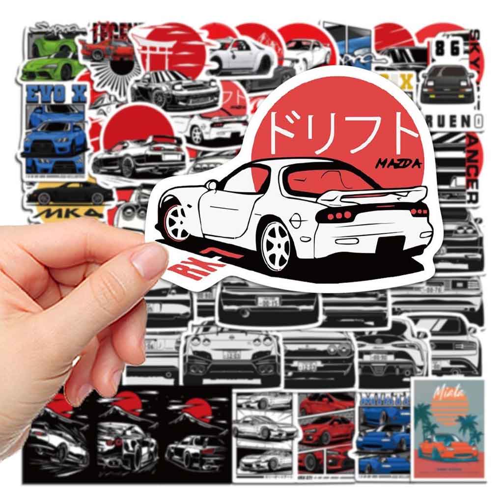 Hand holding a mazda rx7 sticker with lots of different car stickers at background