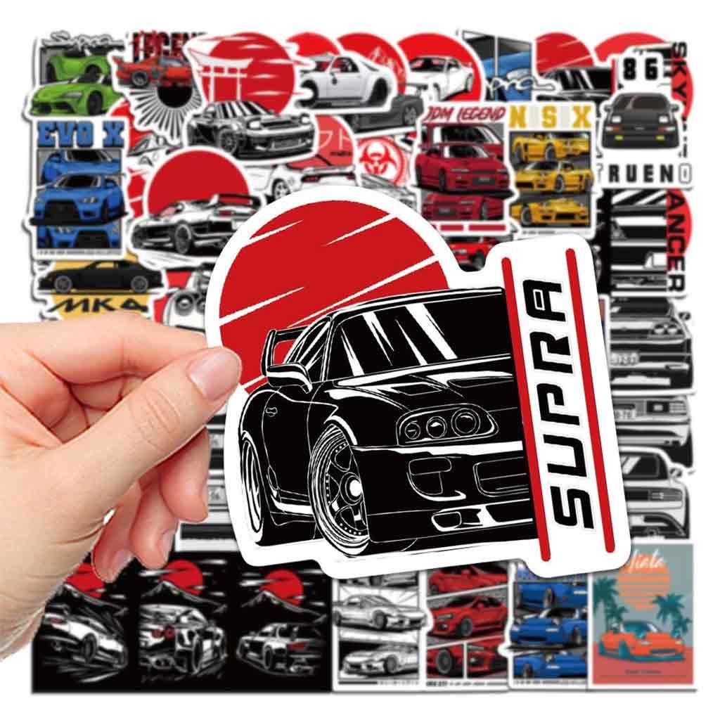 Hand holding a supra sticker with lots of different car stickers at background