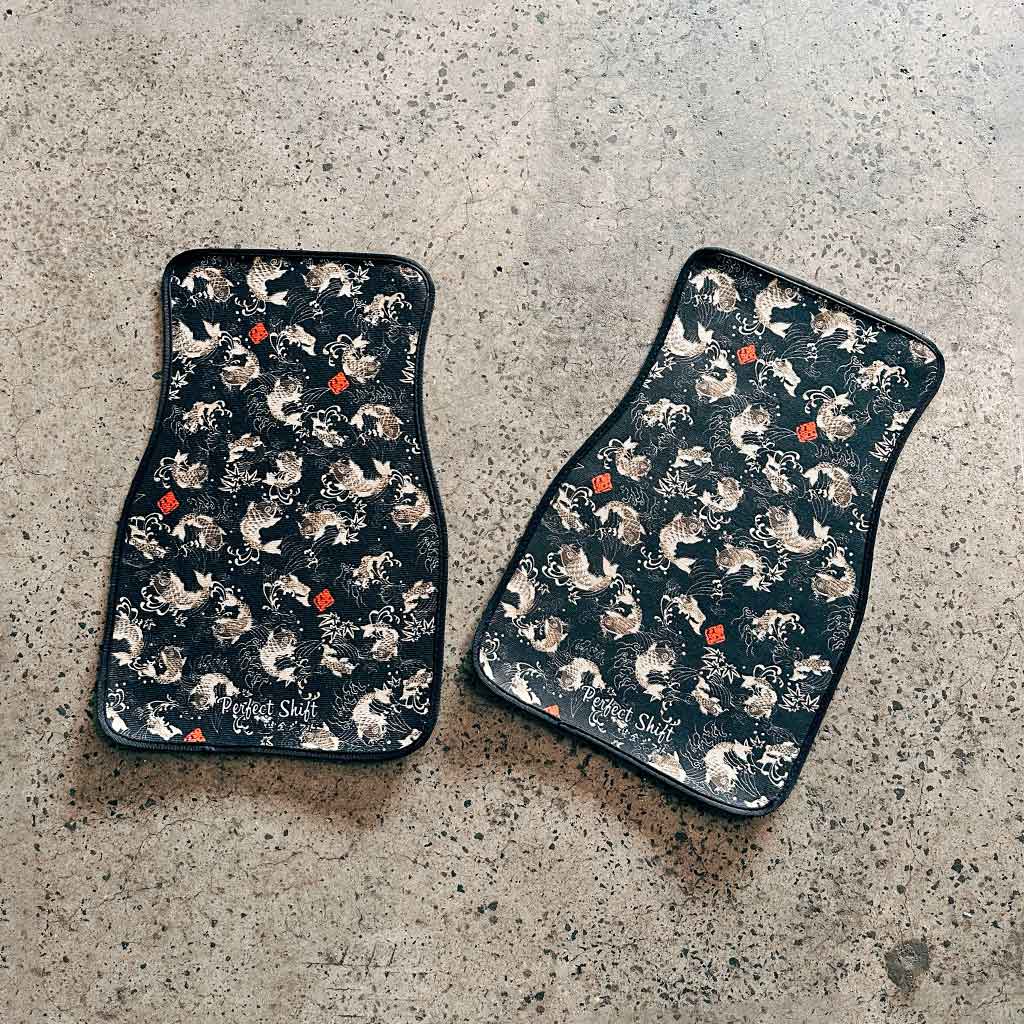 Two pieces of black koi fish JDM floor mat flat laid on a garage ground
