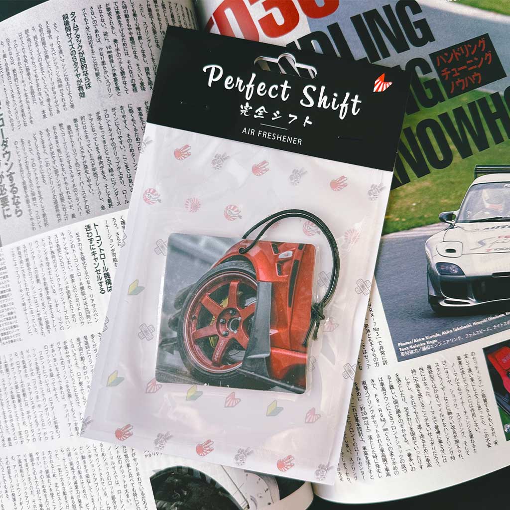 A JDM car air freshener themed TE37 rim flat laid on a Japanese magazine