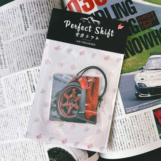A JDM car air freshener themed TE37 rim flat laid on a Japanese magazine