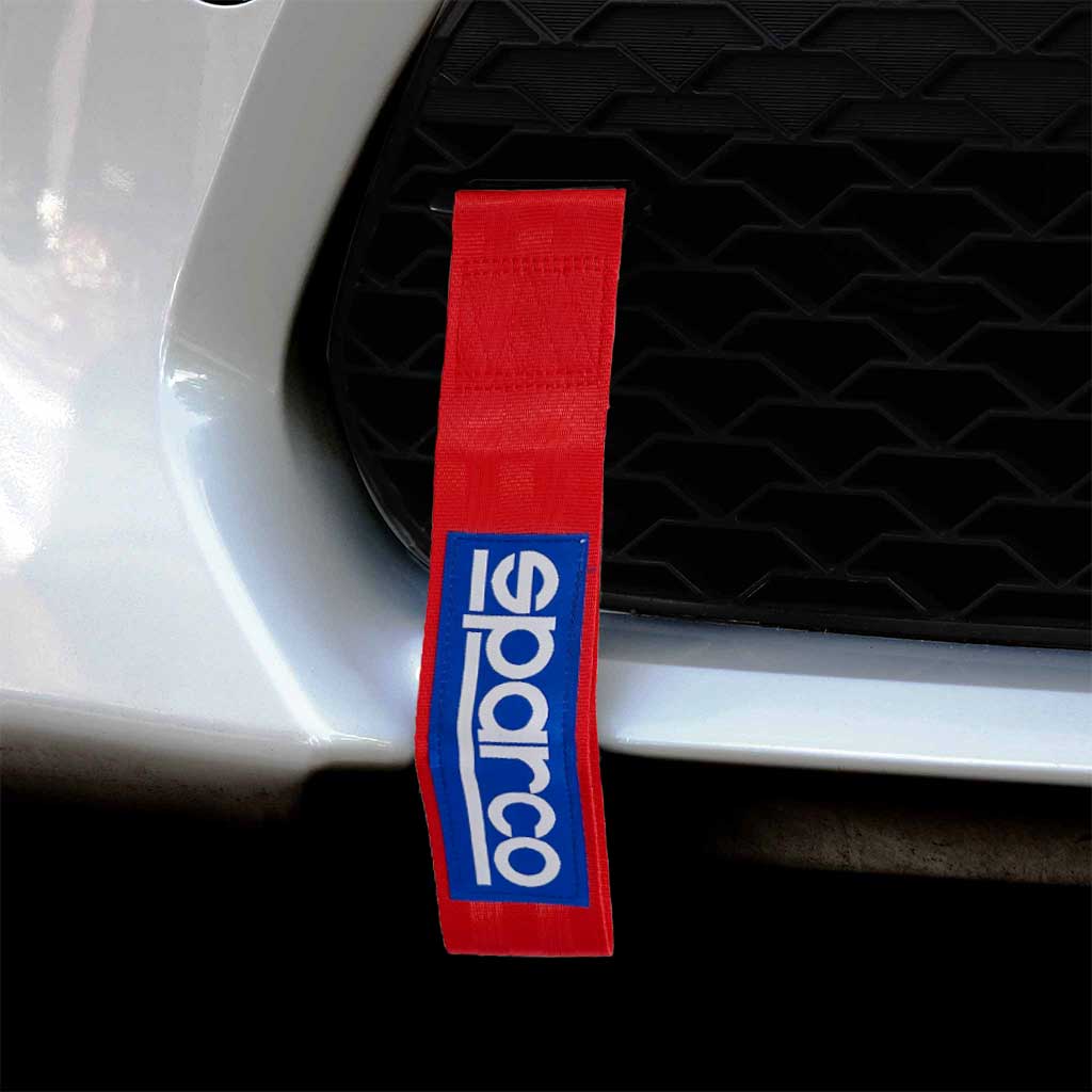 A red Sparco JDM tow strap installed on a white car's front mesh