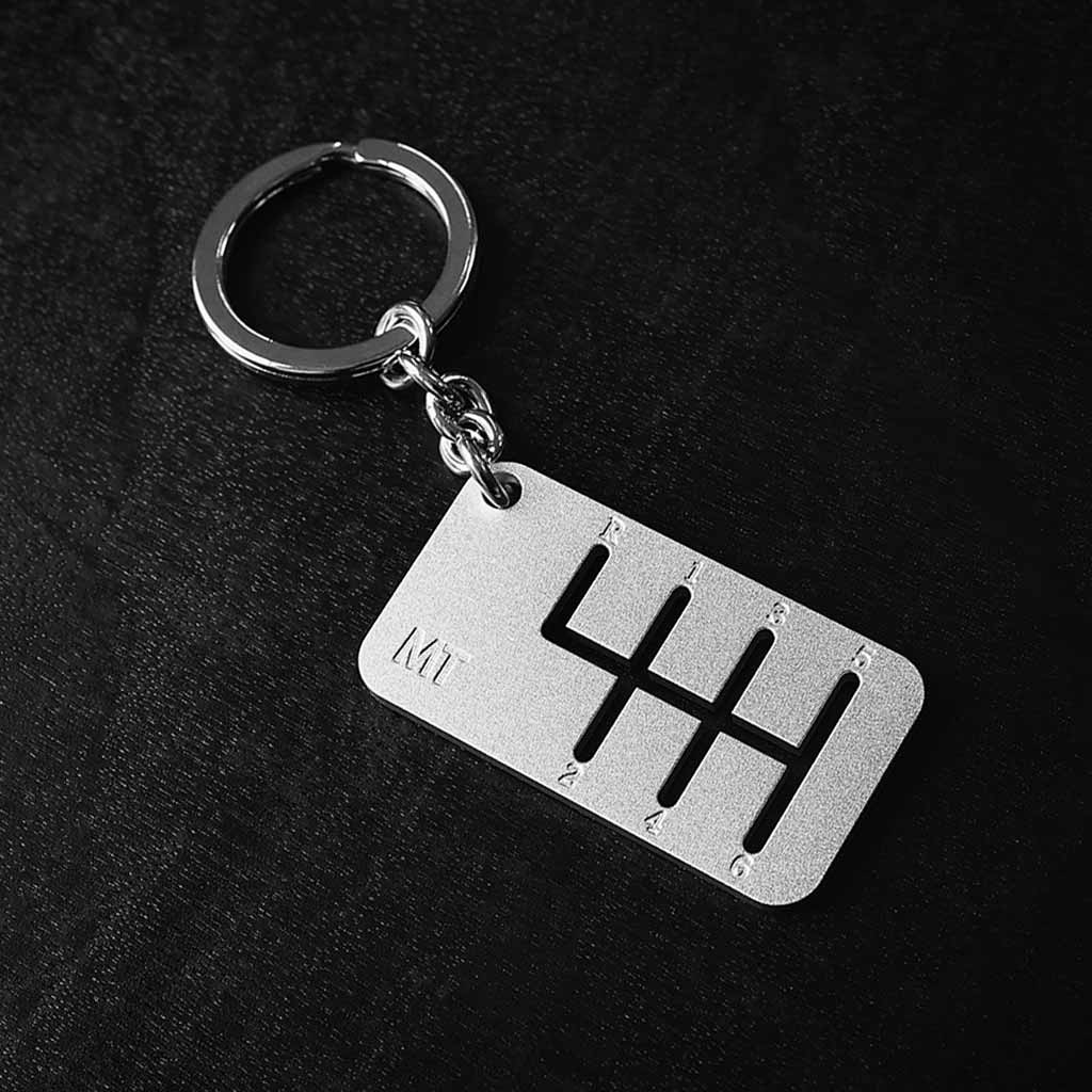 A six-speed manual shift keychain with matte silver finish placed on a black background