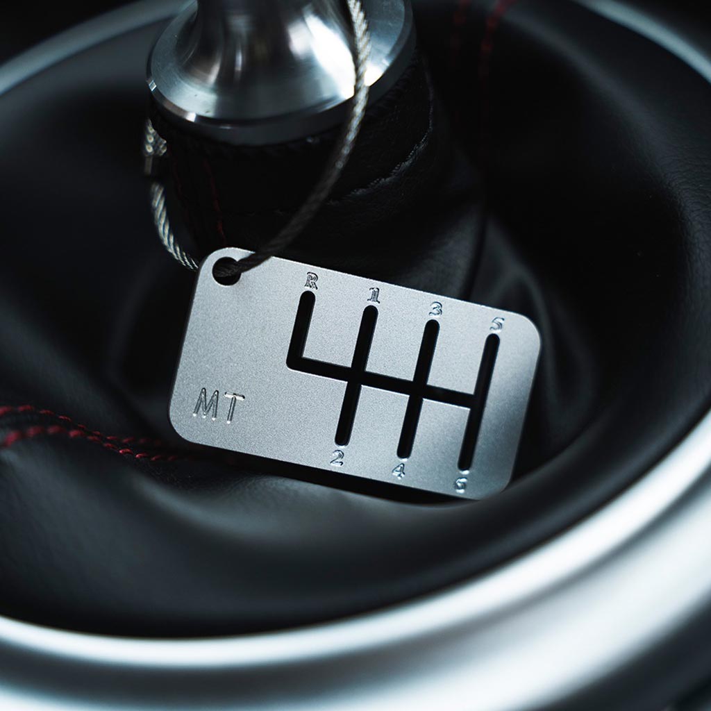 Close-up of a six-speed manual shift keychain with matte silver finish that is hung on a shift boot