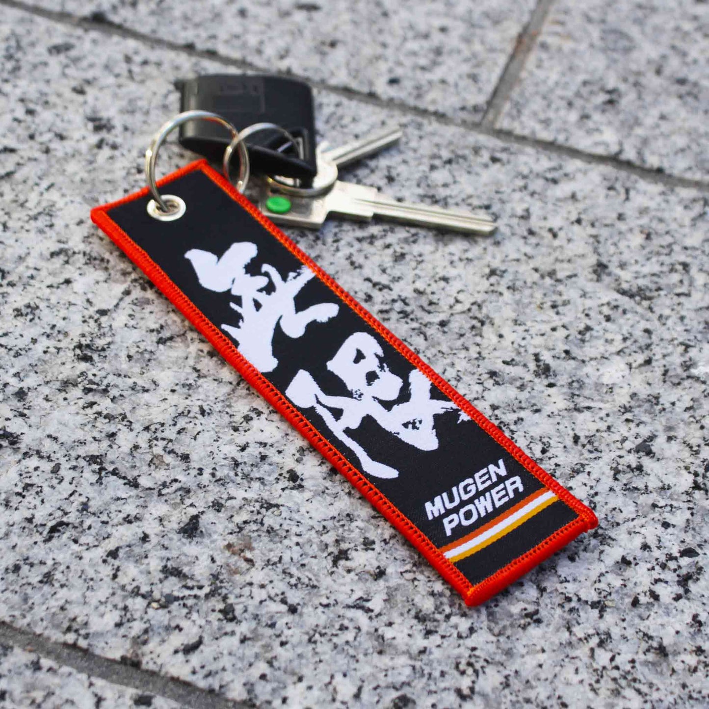A black Mugen power with red outline holding fob and keys on a marble floor