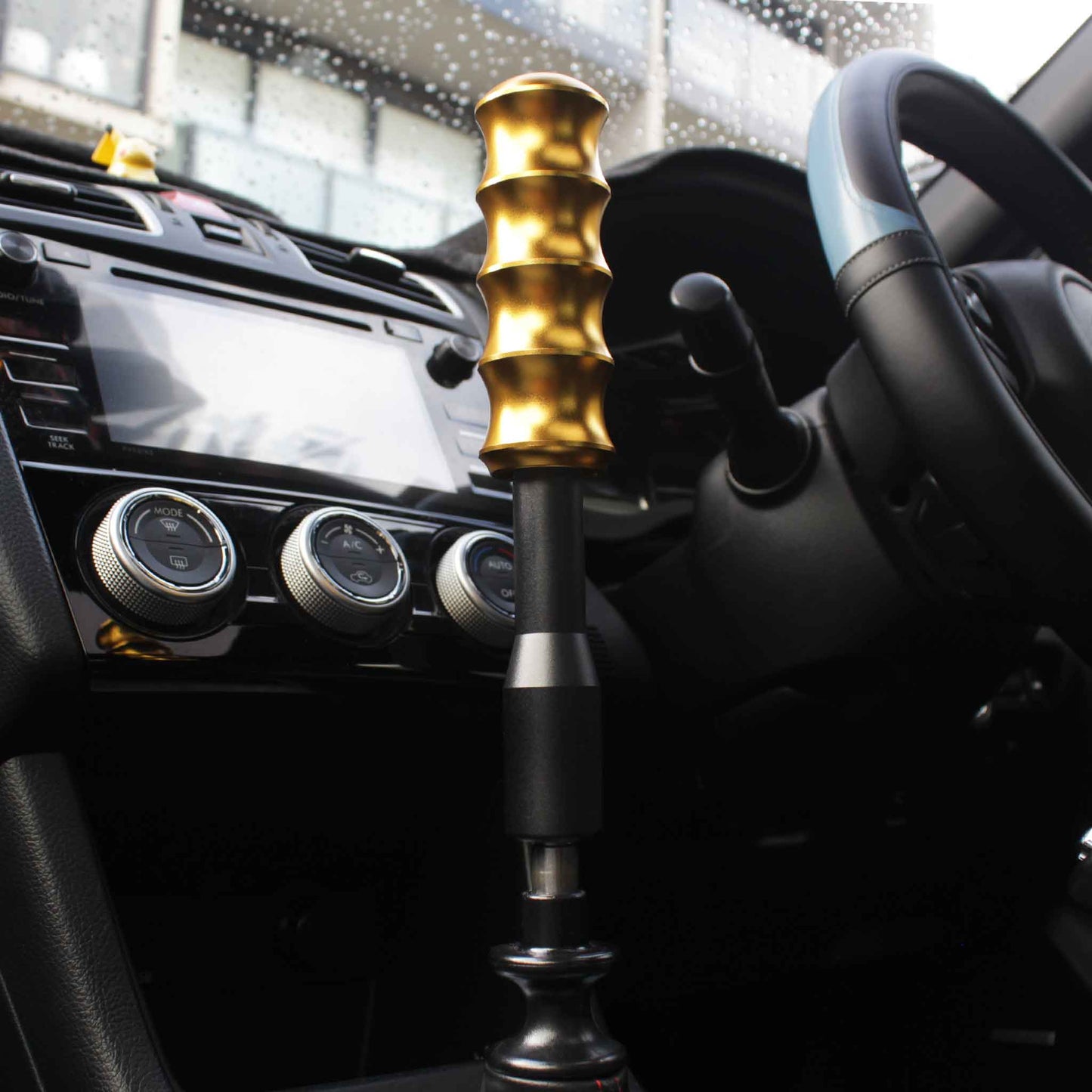 The extension is installed on a manual WRX with a golden Bambooi shift knob, the background being black and white