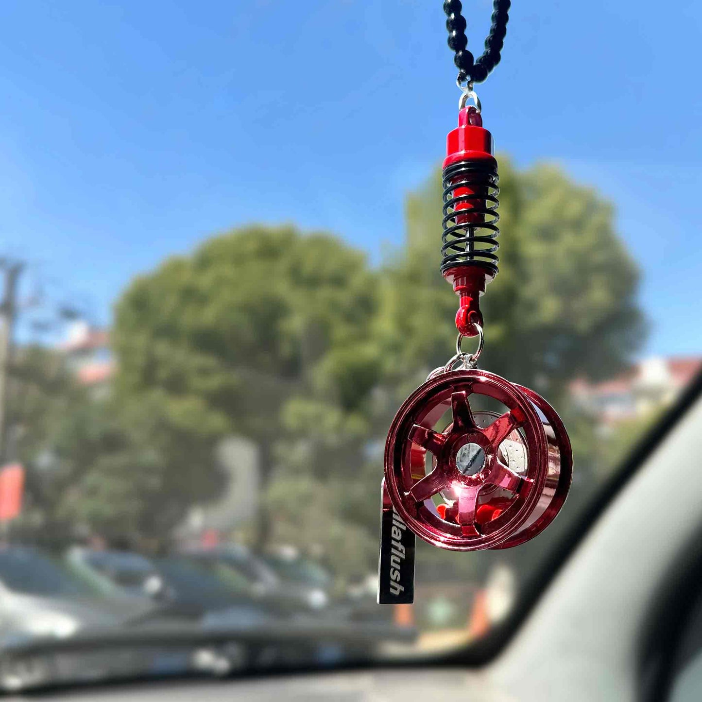 A red wheel decor hung on a car's rearview mirror with blue sky and some cars in the background