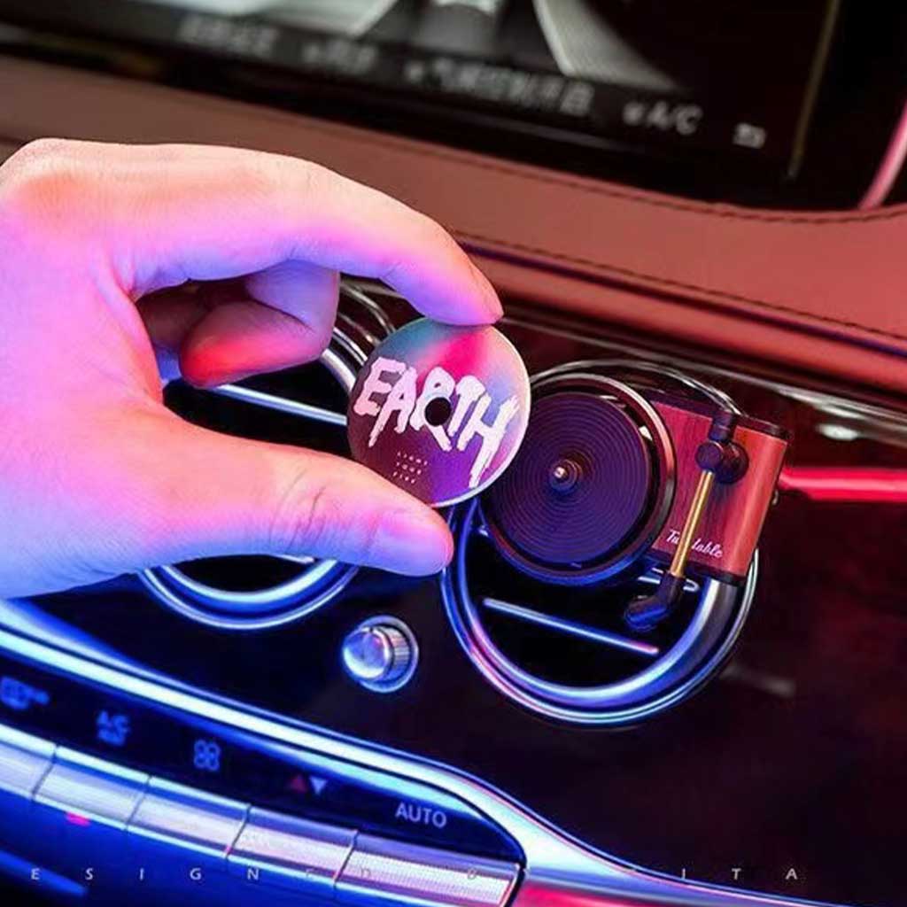 A hand is putting a disc fragrance onto the mini record player air freshener and the air freshener is clipped on a car's air con vents