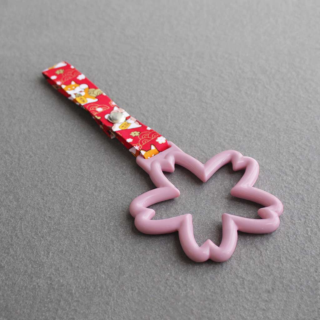 A pink sakura Tsurikawas with maneki-shiba strap flat laid on a concrete floor