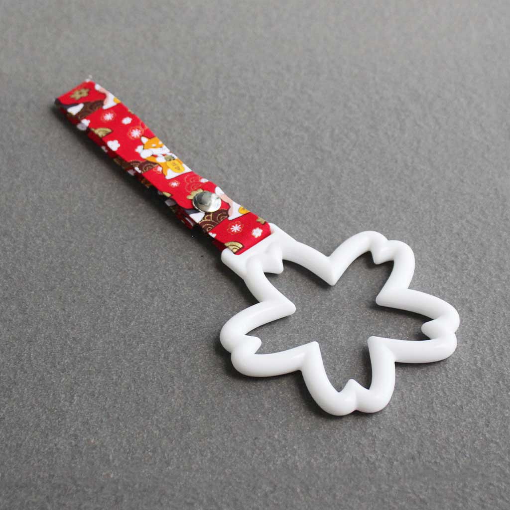 A white sakura Tsurikawas with maneki-shiba strap flat laid on a concrete floor