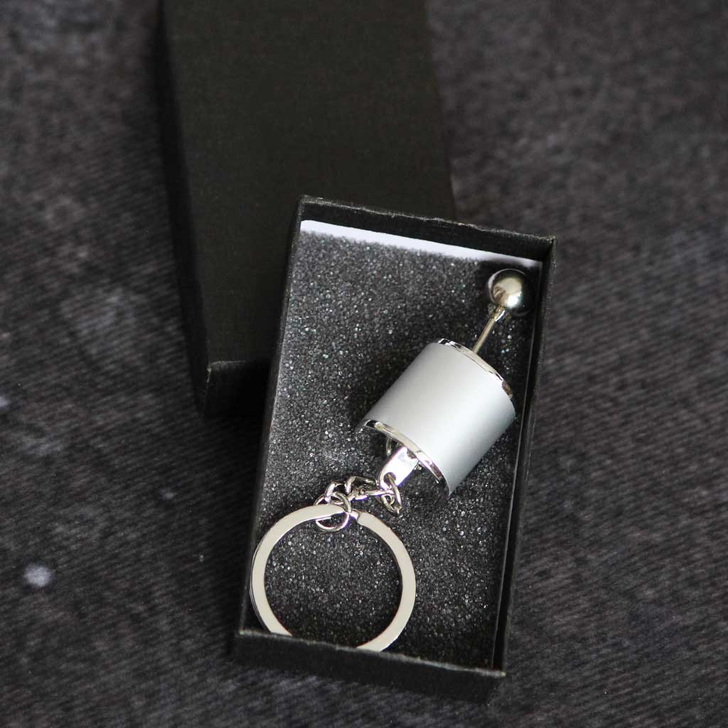 A grey turbo keychain in a black gift box on a grey fabric as background