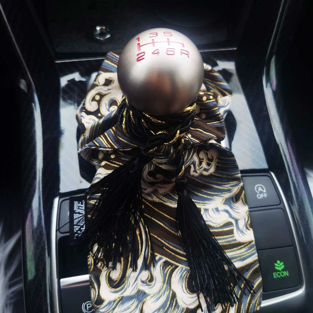 A black waves shift stick cover installed on a car's shift boot underneath a round 6-speed shift knob