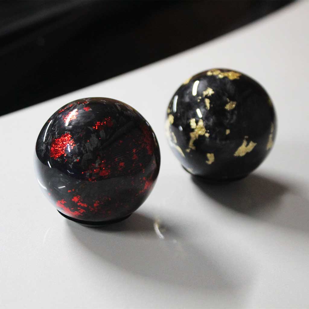 A red shift knob and a black one placed on the hood of a white Toyota 86