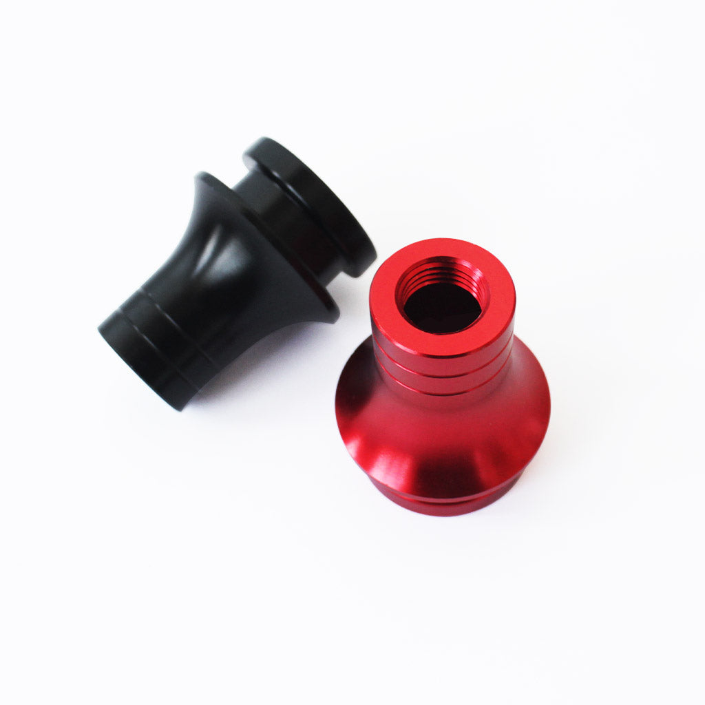 A threaded red boot retainer is standing upright with its top threaded section pointing towards the screen, and a black boot retainer is flat laid on a white background