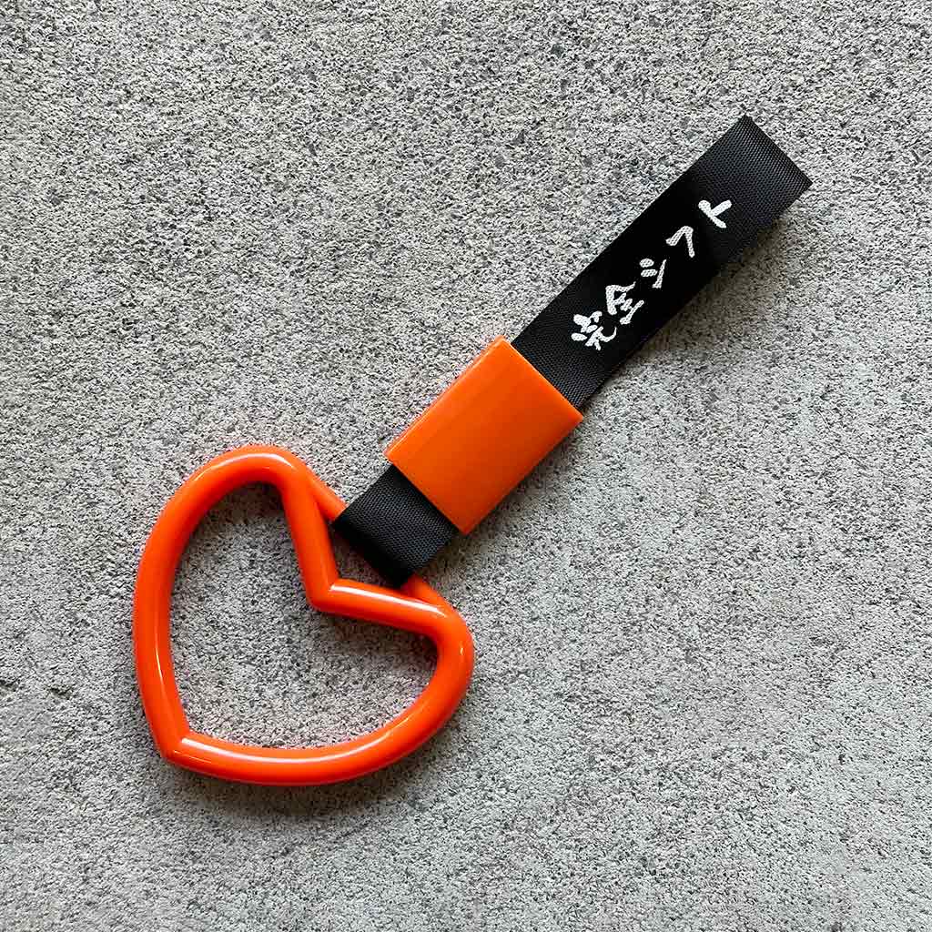 A orange heart Tsurikawa with black strap placed on a concrete ground