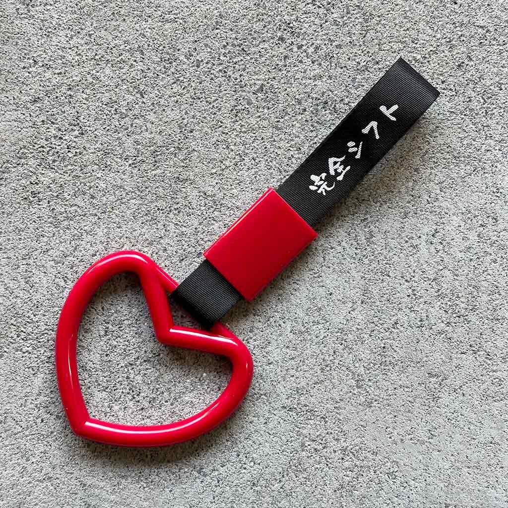 A red heart Tsurikawa with black strap placed on a concrete ground
