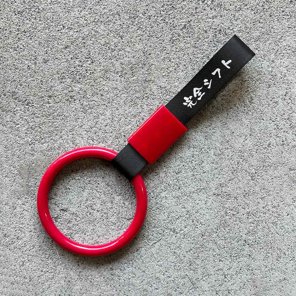 A red ring Tsurikawa with black strap placed on a concrete ground