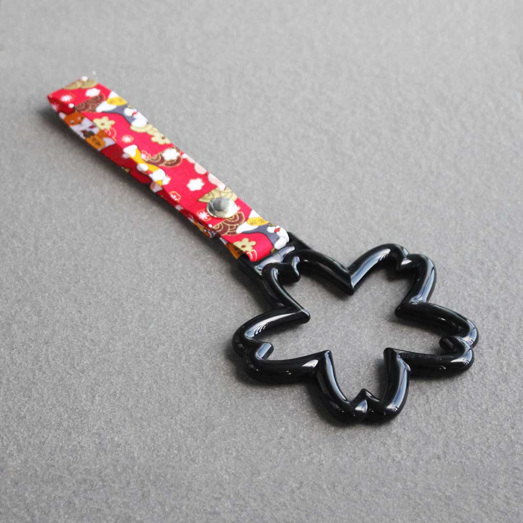 A black sakura Tsurikawas with maneki-shiba strap flat laid on a concrete floor