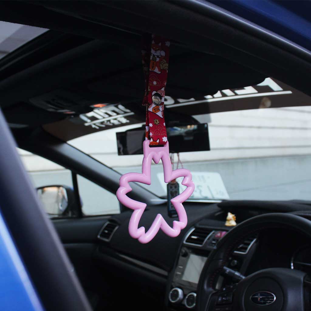 A pink sakura Tsurikawas with maneki-shiba strap hung in a car