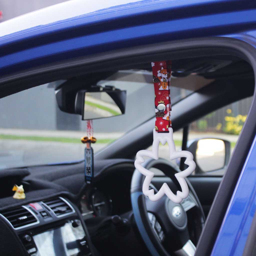 A white sakura Tsurikawas with maneki-shiba strap hung in a car