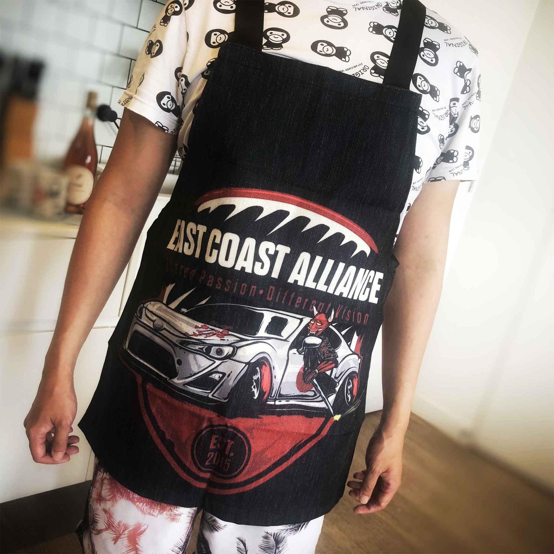 A man wearing a black Toyota-86-themed apron with writings 'East Coast Alliance', standing in the kitchen