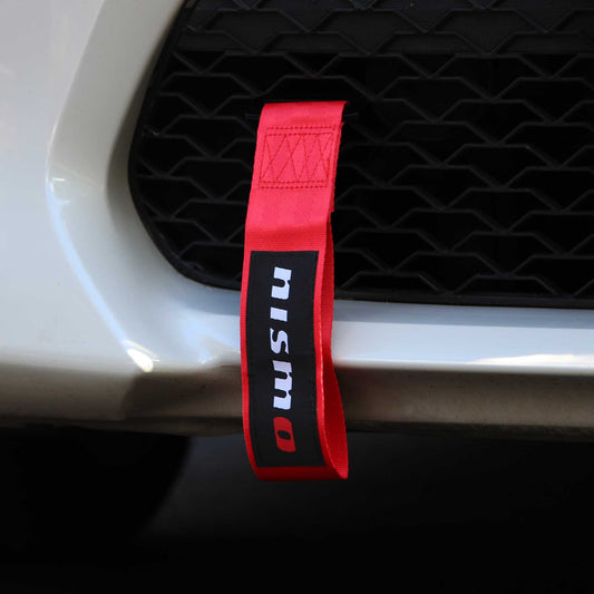 A red nismo tow strap installed on a white car's front grill