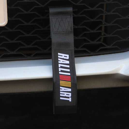 A black ralli-art tow strap installed on a white car's front grille