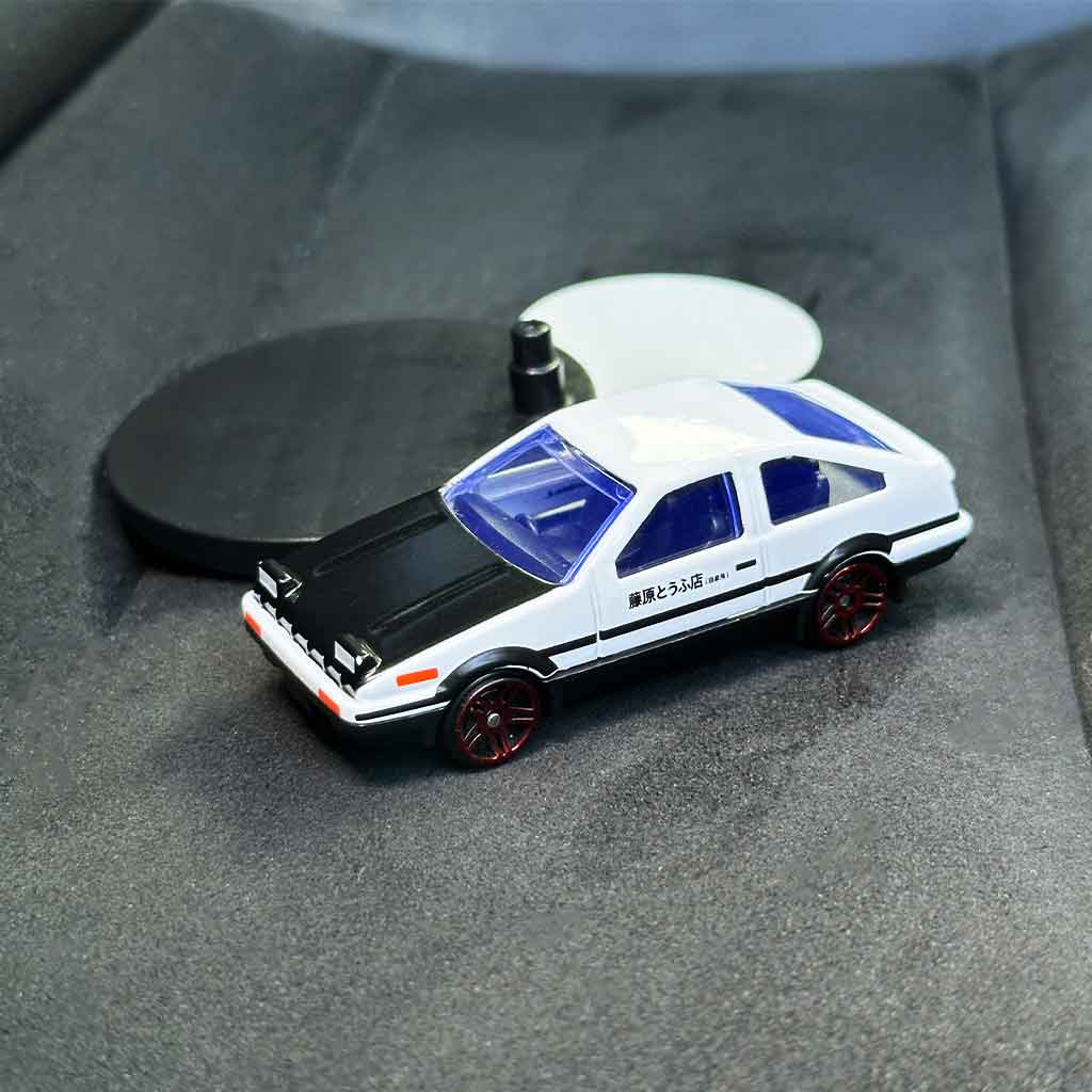 An AE86 car model drifter placed on a 86's seat together with its base and adhesive tape 