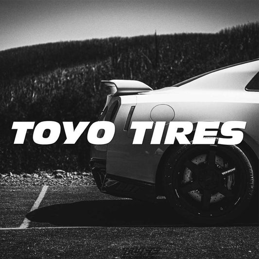A white TOYO TIRES car vinyl decal horizontally placed pointing to the screen with a darkened Skyline R35 at the back