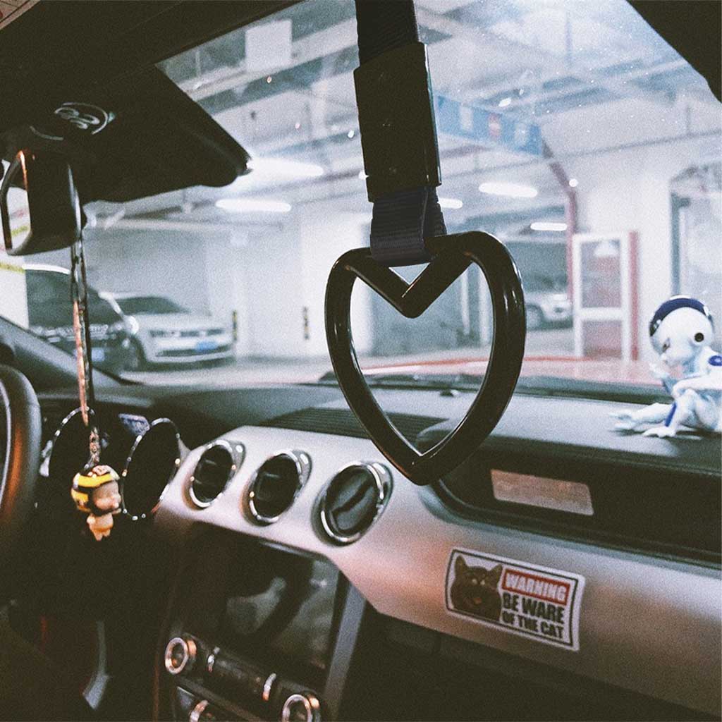 A black heart tsurikawa hung in a car, where a little baby decoration hung on the rearview mirror and a robot toy placed on the center console