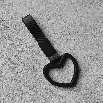 A black heart tsurikawa with black handle strap flat laid on a concrete floor