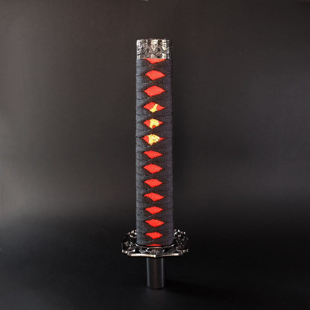 A black and red katana shift knob is standing upright on a dark grey background