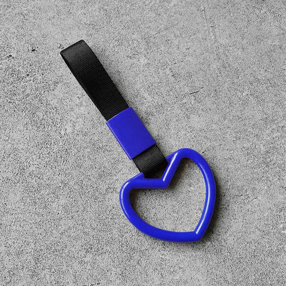 A blue heart tsurikawa with black handle strap flat laid on a concrete floor