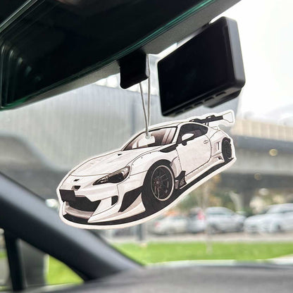 A wide body BRZ air freshener hung on a car's rearview mirror with the rest objects blurred